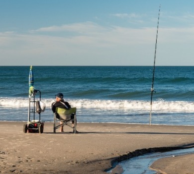 man fishing with cart and poles on beach | Coastline Realty Vacations